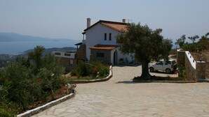A stone house with a tiled roof, a paved driveway, and a view of the sea and mountains in the background. - "Villa Erifili" Luxurious villa with spectacular view in Skiathos Island (Taxiarchis)