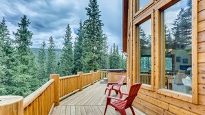 Terraza de madera con sillas rojas, con vista a un área boscosa.