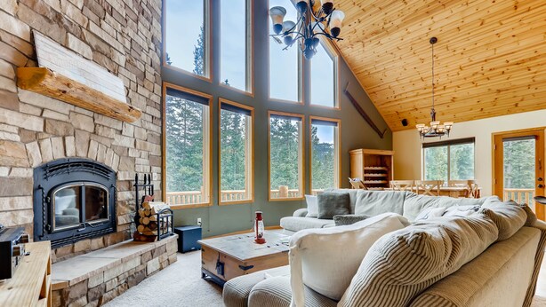Una sala de estar acogedora con chimenea de piedra, ventanas amplias y techo de madera.