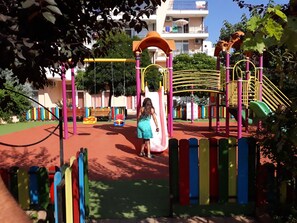Children can play on swings, slides, and climbing areas within a fenced playground.