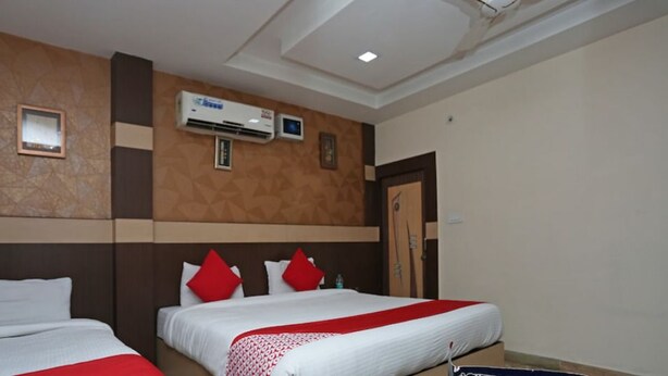 A hotel room with two beds, each with white bedding and red accents, a wall-mounted air conditioner, and a framed picture on the wall. - Hotel Crystal Inn (Lucknow)