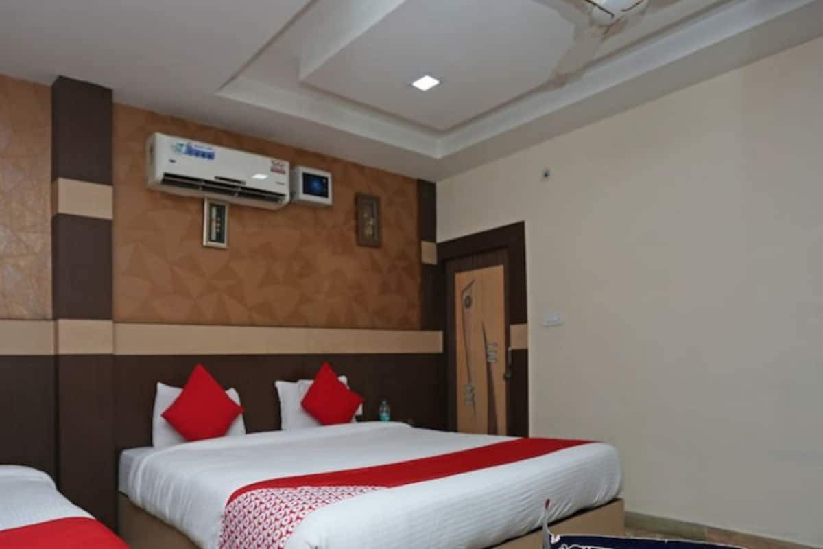 A hotel room with two beds, each with white bedding and red accents, a wall-mounted air conditioner, and a framed picture on the wall.