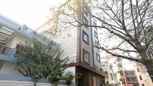 A multi-story building with a modern facade, a staircase leading to the entrance, and a tree in the foreground. - Hotel Crystal Inn (Lucknow)