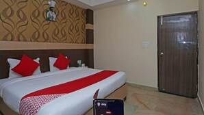 A hotel room with a bed, a ceiling fan, a patterned wall, and a wooden door. - Hotel Crystal Inn (Lucknow)