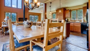 Une salle à manger spacieuse avec une table et des chaises en bois, un lustre et de grandes fenêtres.