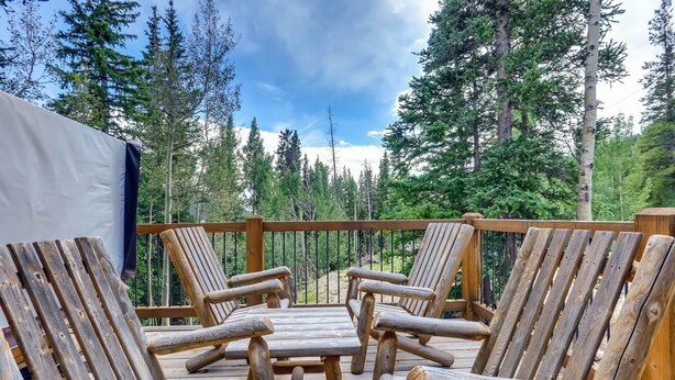Une terrasse en bois avec quatre fauteuils en bois et une table, entourée de grands arbres et surplombant un ciel dégagé.