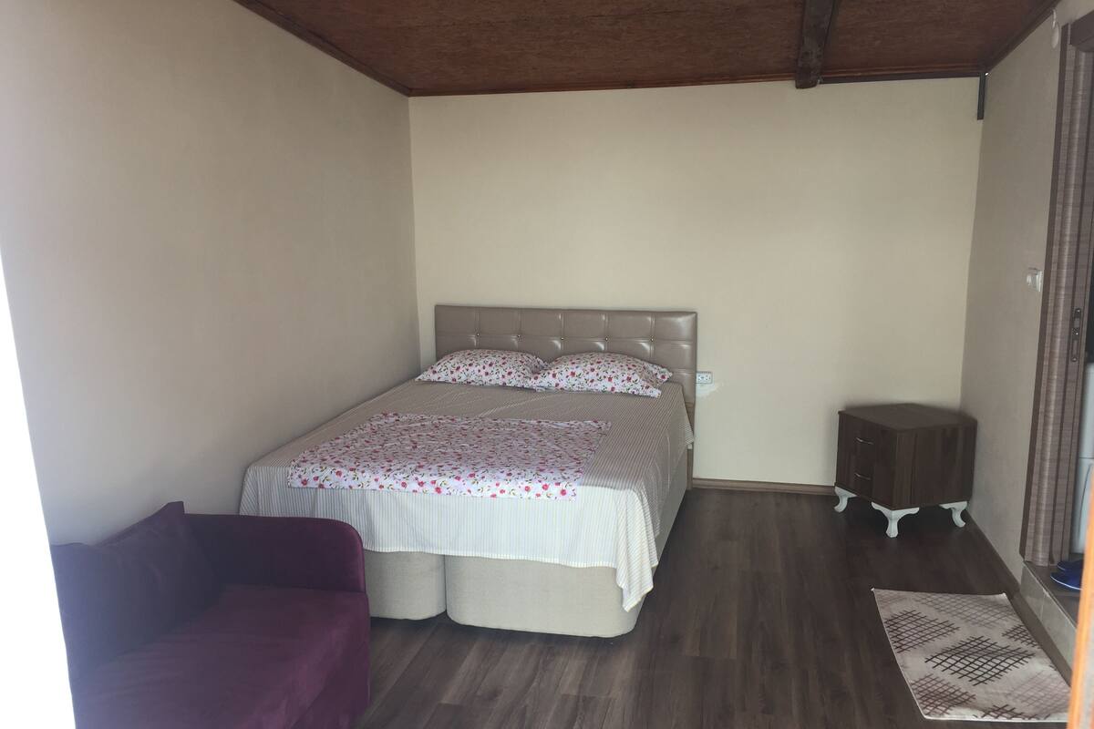 A bedroom with a bed, a small wooden nightstand, a purple sofa, and a patterned rug.