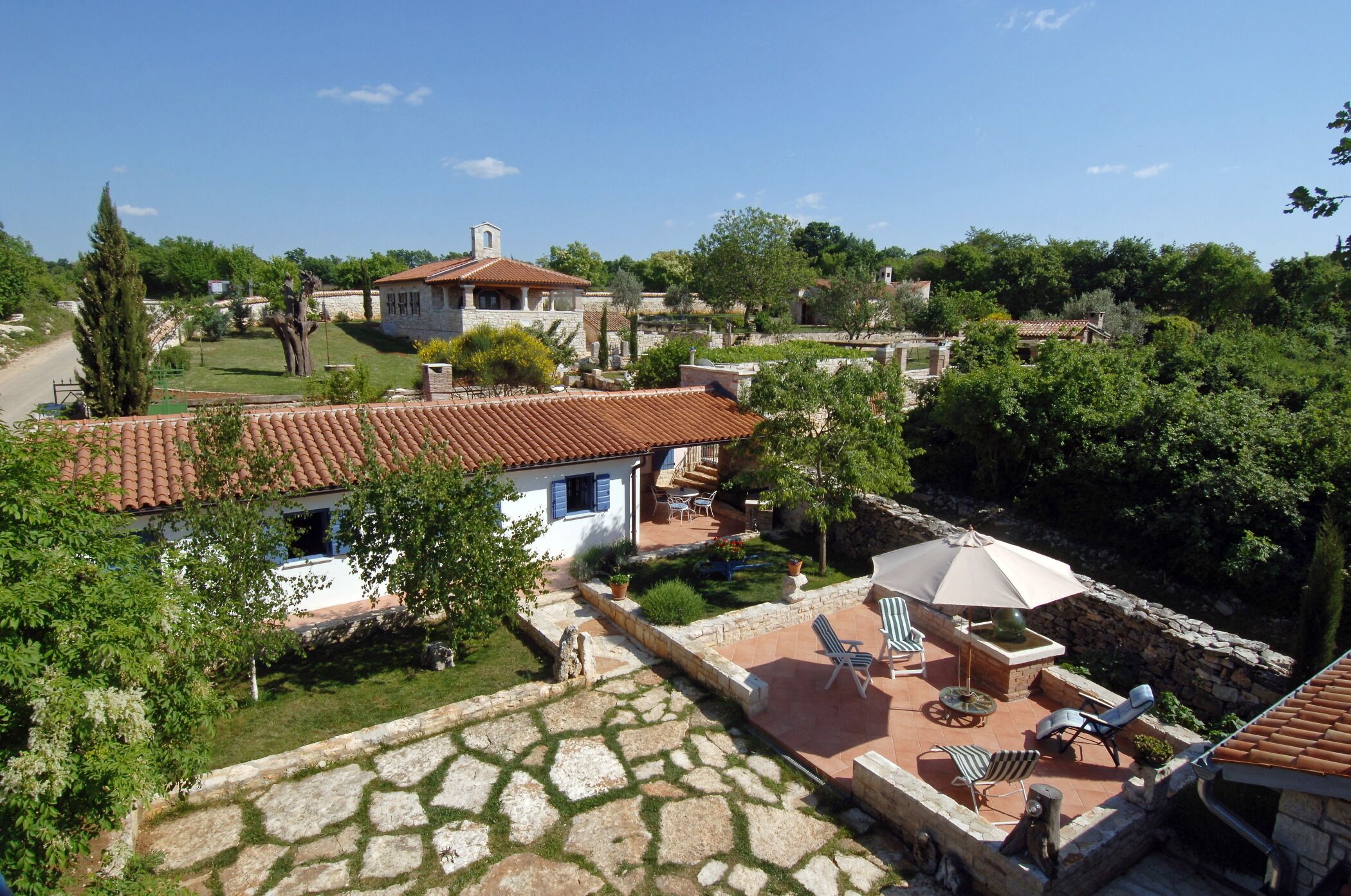Una villa con tejado de baldosas, un patio con mobiliario exterior y un jardín con un sendero de piedra.
