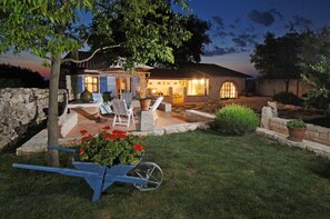 Une maison en pierre avec un patio, un espace salon extérieur et une brouette remplie de fleurs.