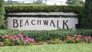 Et skilt med ordet 'BEACHWALK' omgivet af grønt og blomster.