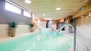 Piscina interior com teto e paredes de madeira, um relógio e plantas em vasos.