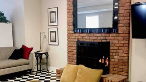 A living room with a brick fireplace, a sofa, a coffee table, and framed pictures on the wall. - Cozy Suite on Cedars 1300sq ft (ONE LEVEL) (Hickory)