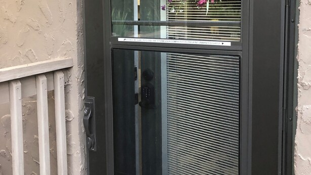 A door with a glass panel and a metal grill, a white doorbell, and a sign above the door. - Cozy Suite on Cedars 1300sq ft (ONE LEVEL) (Hickory)