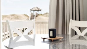 A table with a black mug on a coaster, white chairs, and a view of the beach and dunes in the background. - Bear Inn OBX - 4X4 Carova Beach, Oceanfront, Ocean View, Hot Tub, Pets OK (4X4 - Carova Beach)