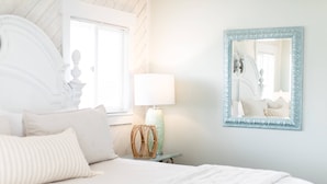 A bedroom with a bed, a lamp, a mirror, and a window. - Bear Inn OBX - 4X4 Carova Beach, Oceanfront, Ocean View, Hot Tub, Pets OK (4X4 - Carova Beach)