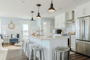 Une cuisine moderne avec des meubles blancs, des appareils en acier inoxydable et des luminaires suspendus.