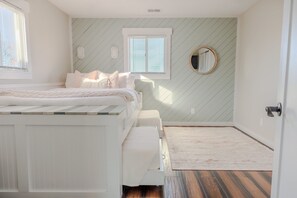 A bedroom with a bed, a bedside table, a mirror, and a window with blinds. - Bear Inn OBX - 4X4 Carova Beach, Oceanfront, Ocean View, Hot Tub, Pets OK (4X4 - Carova Beach)