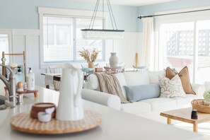 Un soggiorno moderno con un divano bianco, un tavolino in legno e un angolo cottura illuminato da un lampadario a sospensione.