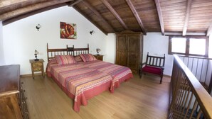 Ein Schlafzimmer mit Holzboden, einem großen Bett mit gemusterten Textilien, einem Holzschrank und einem Sessel.