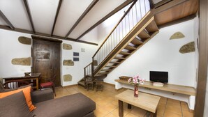 Ein Wohnzimmer mit einer Couch, einem Holztisch, einem Fernseher auf einem Regal und einer Treppe.