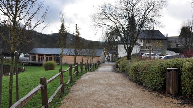 A gravel path leading to a building with a sloped roof, surrounded by trees and a wooden fence.
