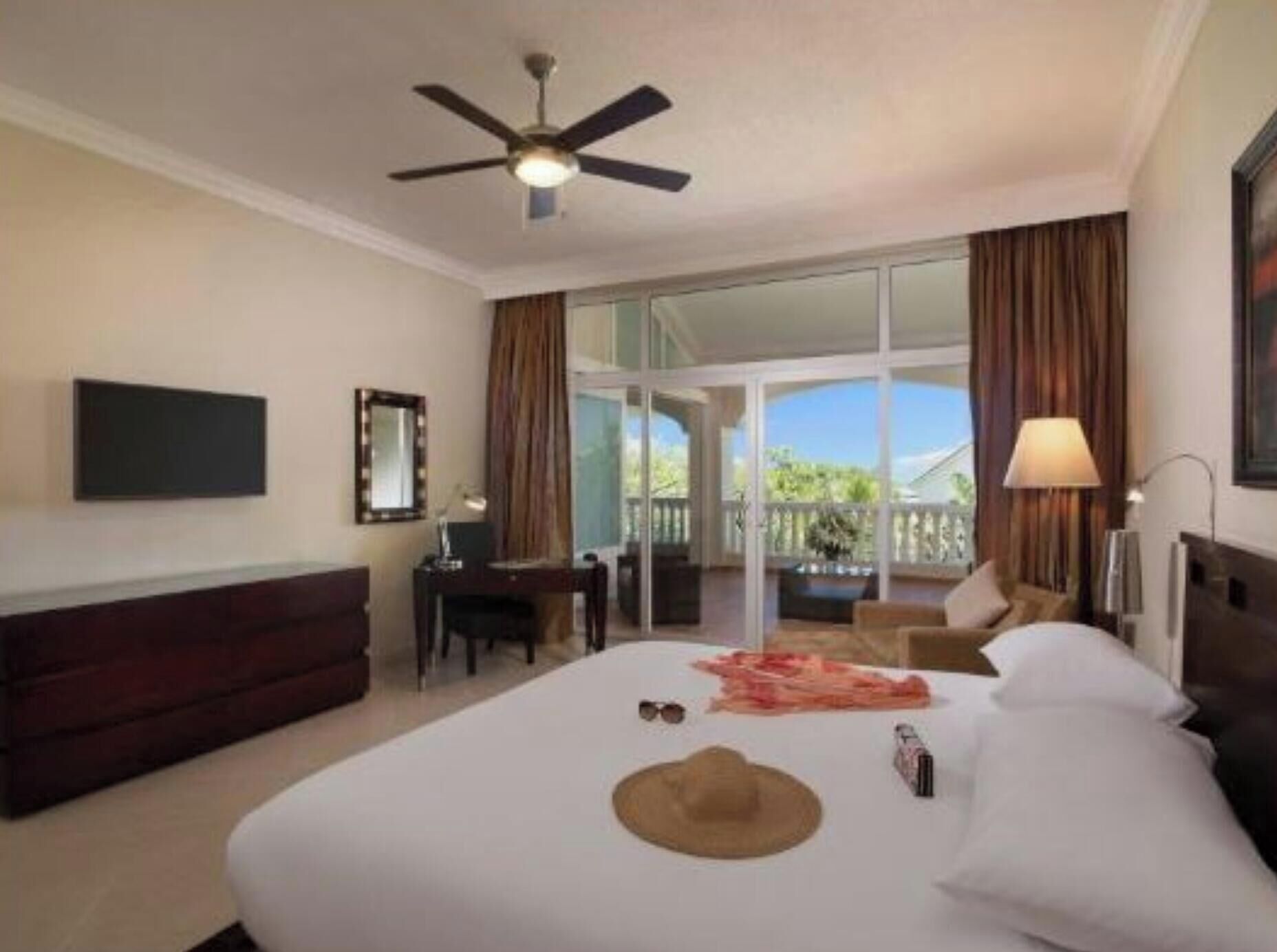 A hotel room with a bed, a desk, a chair, a TV, and a ceiling fan.