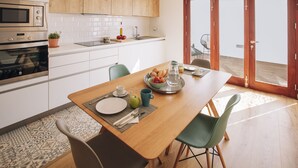 Uma cozinha moderna com armários brancos, forno de aço inoxidável e uma área de jantar com mesa de madeira e cadeiras verdes.