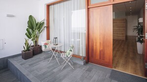 Um interior moderno com porta de vidro deslizante, uma pequena mesa com cadeiras e plantas em vasos.