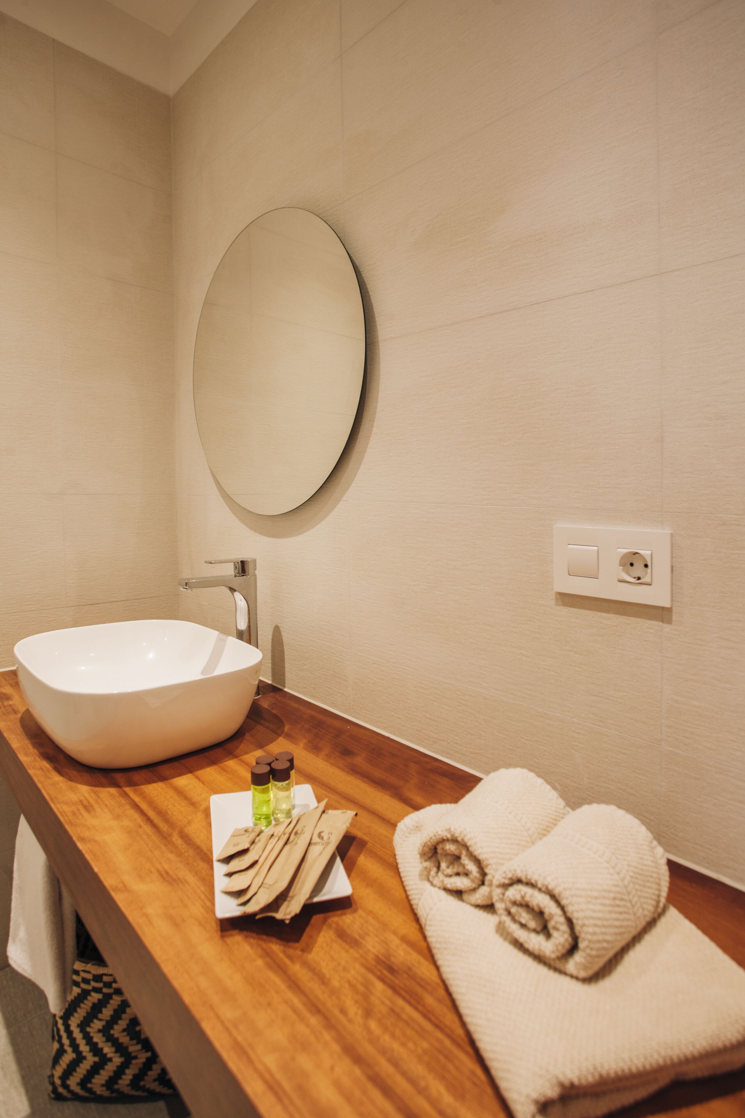 A bathroom with a white sink, wooden countertop, a mirror, and towels.