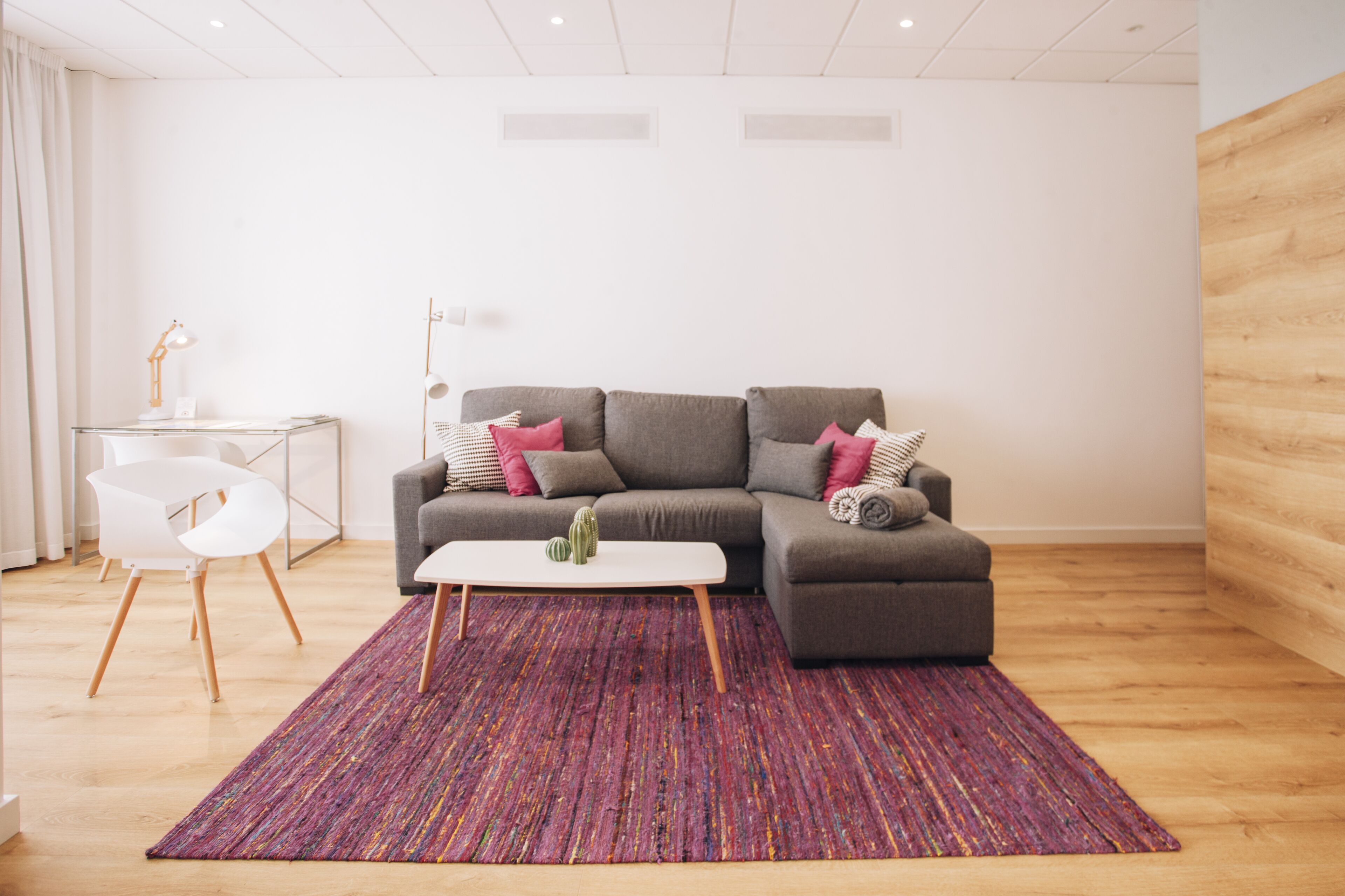 Un salon moderne avec un canapé d’angle gris, une table basse blanche et un tapis coloré.