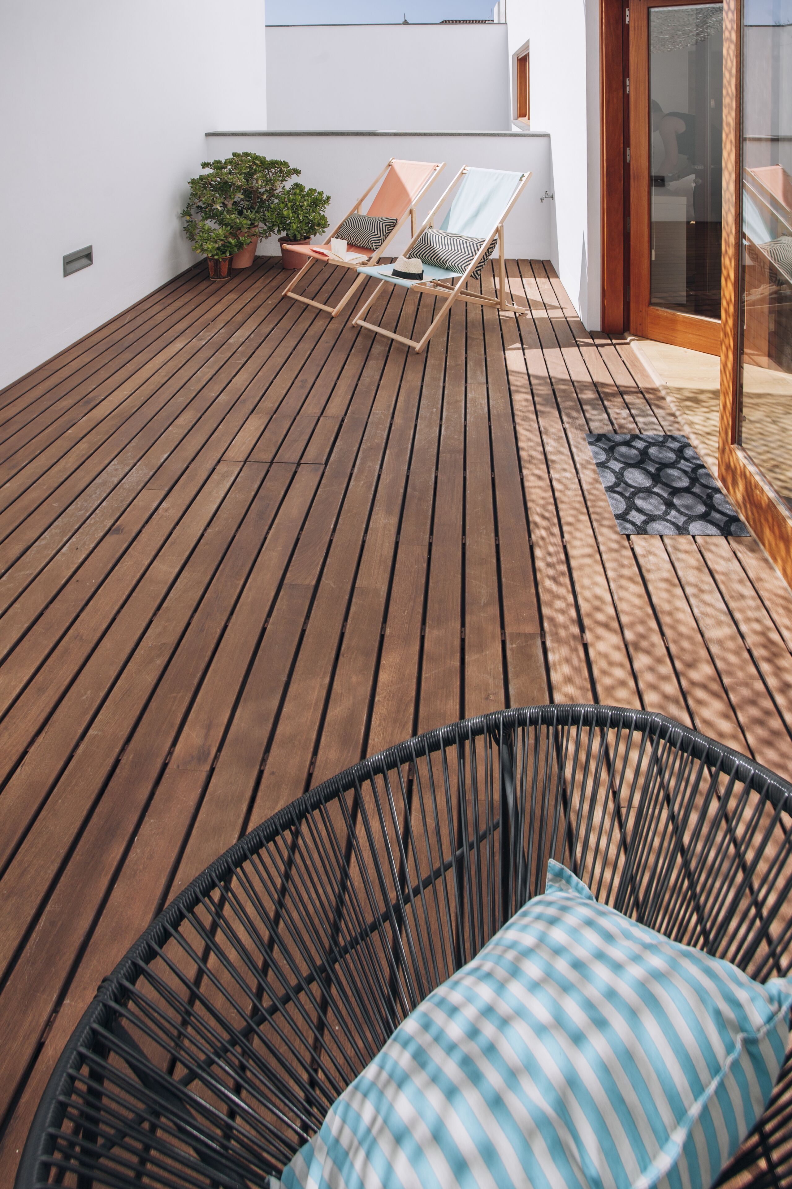 Una terraza de madera con sillones de descanso y una planta en maceta.