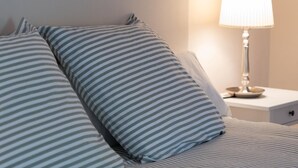 A neatly made bed with striped pillows and a bedside lamp on a white nightstand.