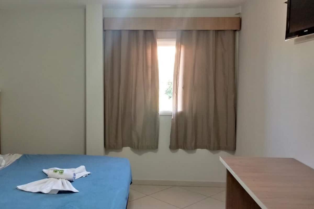 Una habitación de hotel con una cama, un cabecero de madera, una ventana con cortinas y un televisor de pantalla plana montado en la pared.