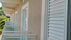 A row of hotel rooms with white shutters and a beige exterior wall. - Hotel Canaã Express (Jarinu)