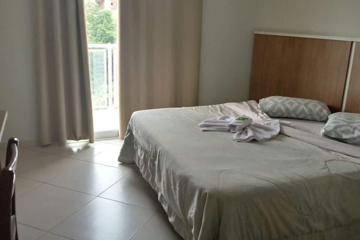 Habitación de hotel con cama, cabecera de madera y vista a zonas verdes.