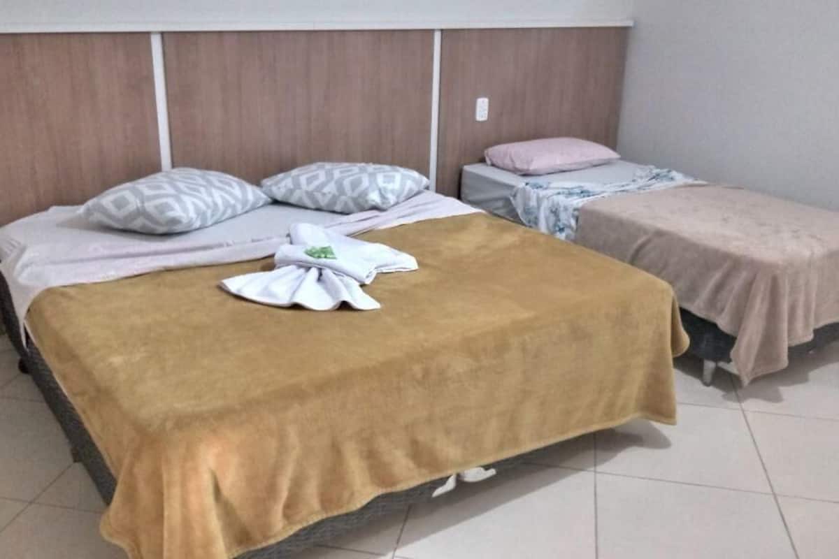 Una habitación de hotel con una cama grande, una cama más pequeña y una sola mesita de noche.