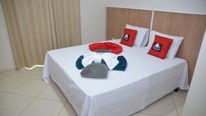 A neatly made bed with white bedding, two red pillows, and a gray pillow. - Hotel Canaã Express (Jarinu)
