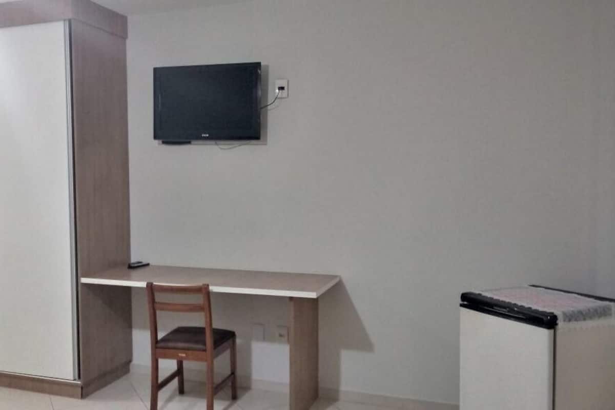 Una habitación con un escritorio, una silla, un armario y una televisión instalada en la pared.