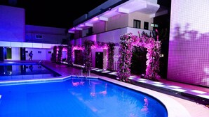 A swimming pool with a purple-lit archway and a building in the background. - Hotel Rio Parnaiba (Floriano)