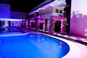 Una piscina con un arco iluminado de color púrpura y un edificio al fondo.