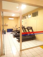 Un gimnasio con equipo de ejercicio, un separador de vidrio y una pared amarilla.