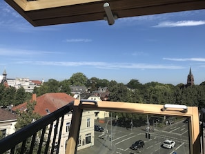 En utsikt från en balkong med utsikt över en stadssiluett med byggnader, träd och ett kyrktorn.