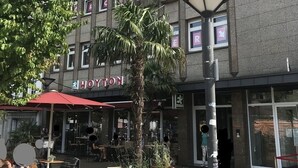 Rakennuksessa on kyltti, jossa lukee ”WOYTON”, ja sen edessä on terassi, jossa on pöytiä ja tuoleja.
