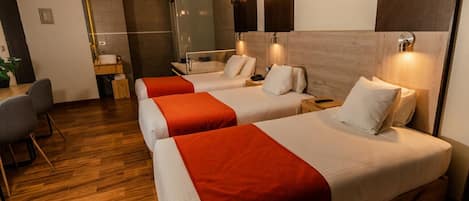 Habitación de hotel con tres camas, piso de madera y decoración moderna.