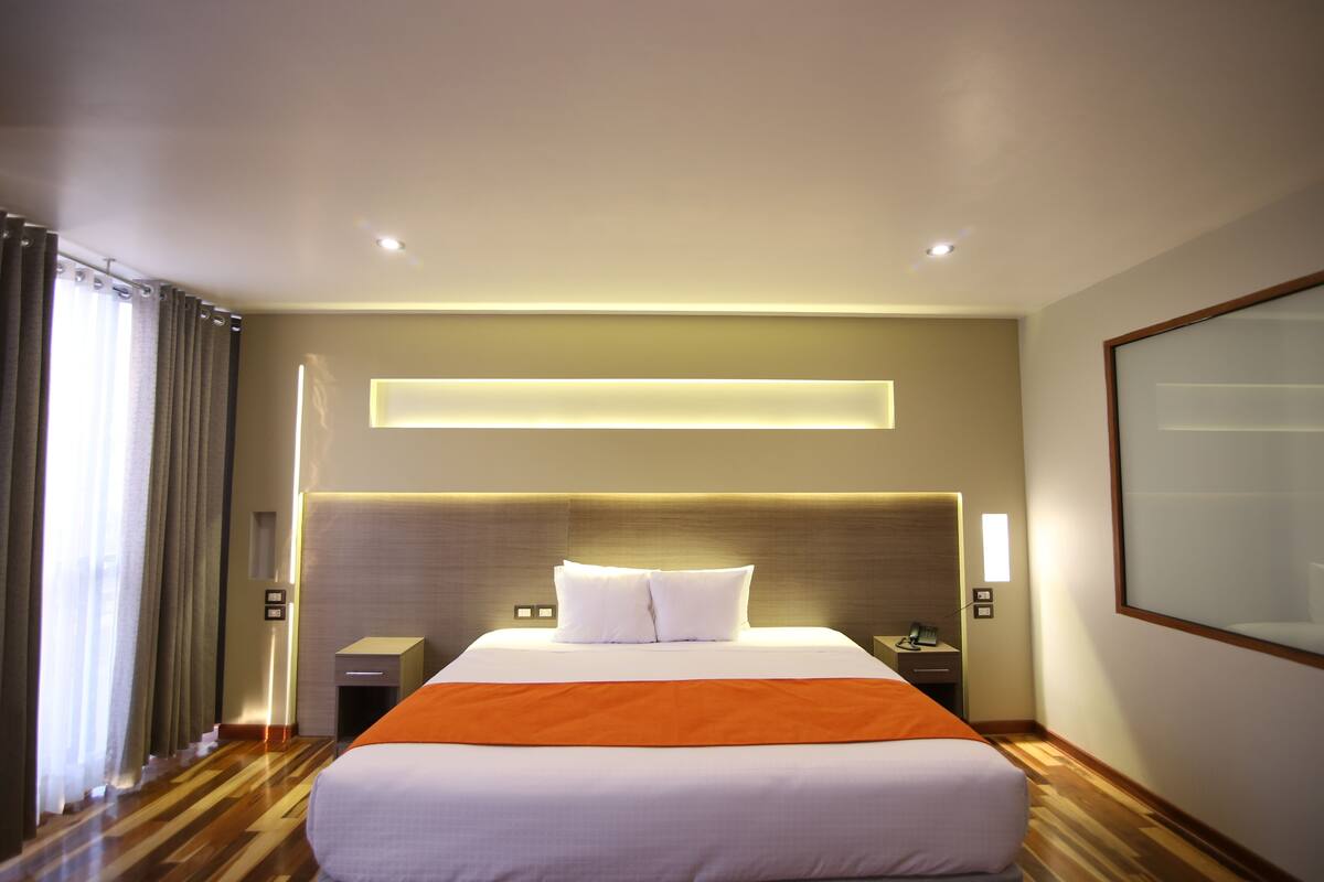 A hotel room with a large bed, a nightstand, a lamp, and a window with curtains.
