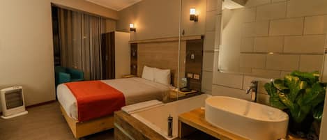 A hotel room with a bed, a large mirror, a sink, and a small heater.