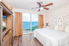 A hotel room with a bed, a ceiling fan, a television, and a view of the sea.