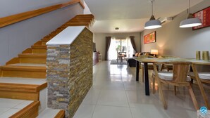 A modern interior with a wooden staircase, a dining area with a wooden table and chairs, and a view of the outdoors through a glass door. - Cozy and spotless 6 guest apartment-great location only 50 steps to Eagle Beach! (Eagle Beach)