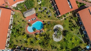 An aerial view of a resort with a central swimming pool, surrounded by palm trees and a red-roofed building. - Cozy and spotless 6 guest apartment-great location only 50 steps to Eagle Beach! (Eagle Beach)
