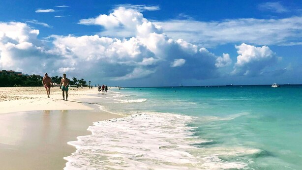 A beach with clear turquoise water, gentle waves, and a few people walking along the shore. - Cozy and spotless 6 guest apartment-great location only 50 steps to Eagle Beach! (Eagle Beach)